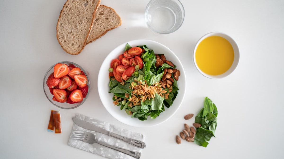 Top view of a healthy salad and fresh ingredients with bread and juice on a white surface.