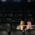 A couple enjoying a movie date with popcorn in an empty theater.